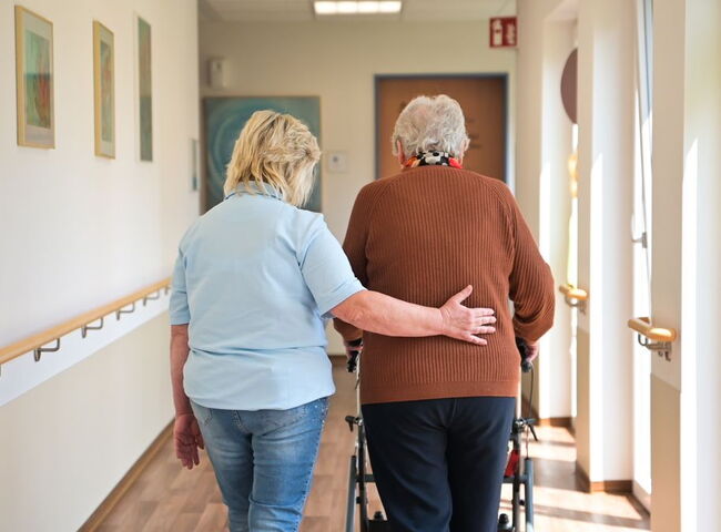 Eine Mitarbeiterin führt eine Bewohnerin über den Flur