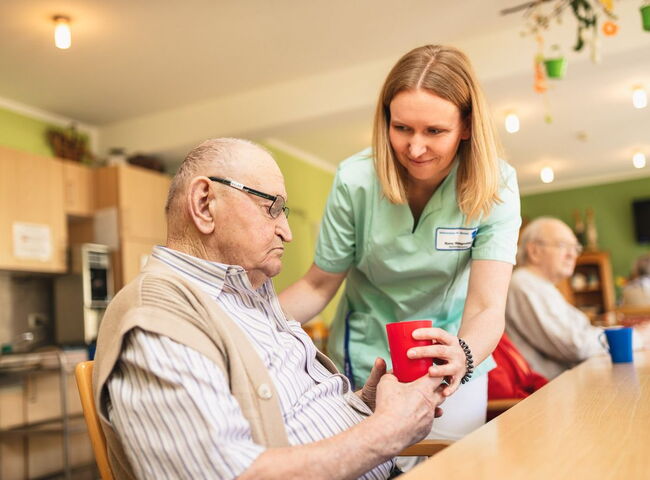 Eine Mitarbeiterin reicht einem Bewohner ein Getränk